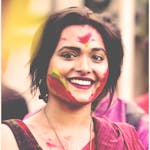 Vibrant portrait of a smiling woman with colorful face paint at Holi festival.